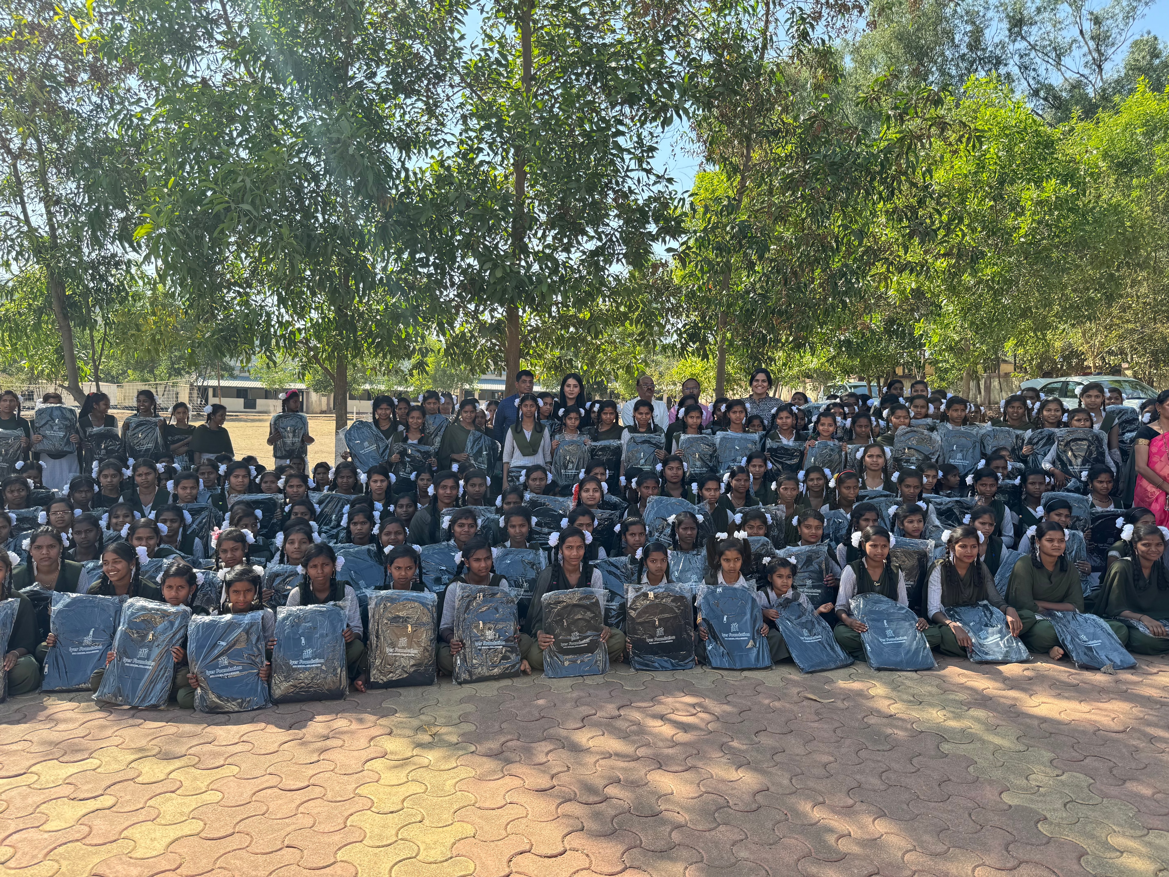 Large group of girls holding Iyer Foundation school bags outdoors under trees