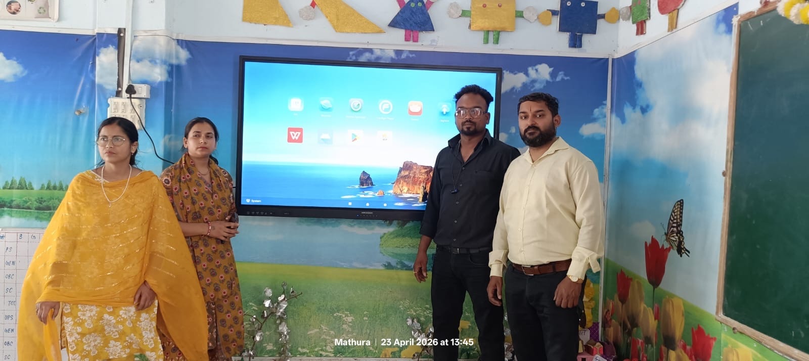 Four people standing in front of a newly installed smart board in a decorated classroom in Mathura