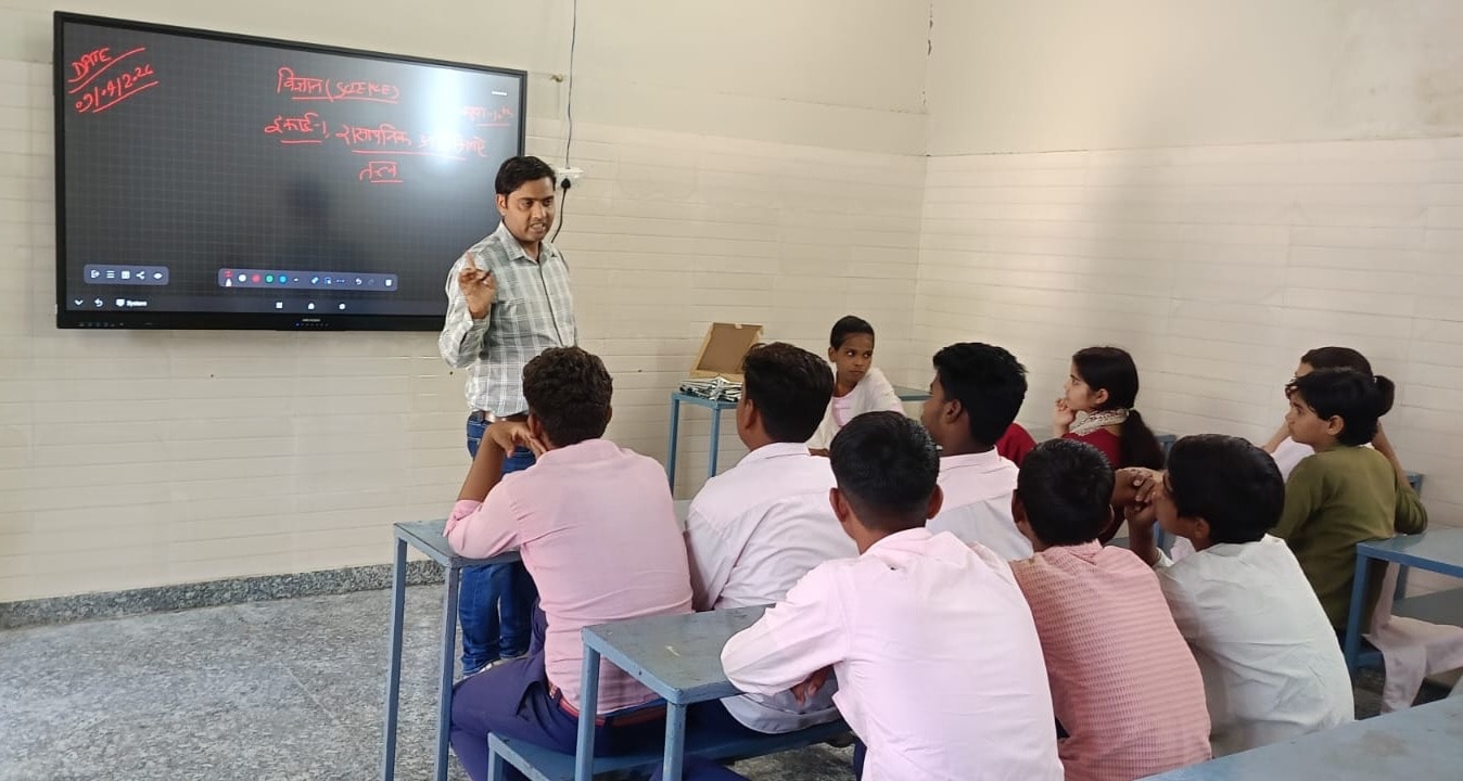 Teacher explaining a lesson to students seated in front of a smart board