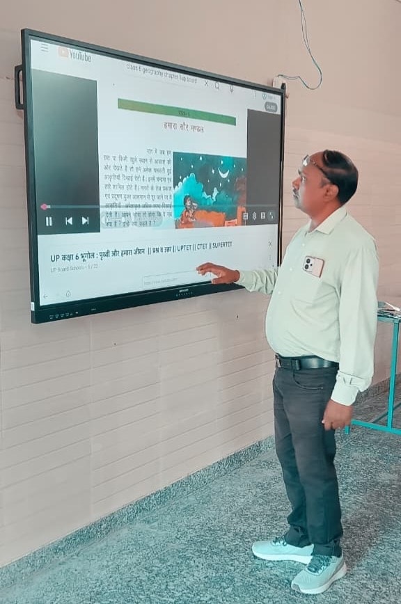 Teacher pointing at educational content on a smart board showing Hindi text